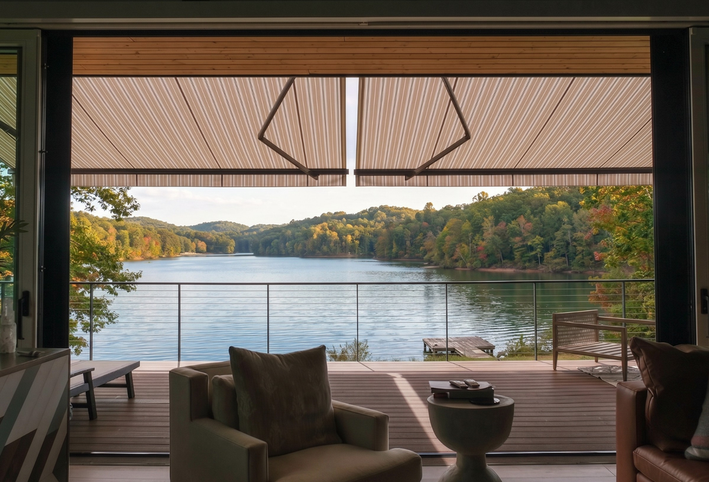 A breathtaking view of a river from a backyard porch, covered by a roof structure and shaded by a retractable awning.